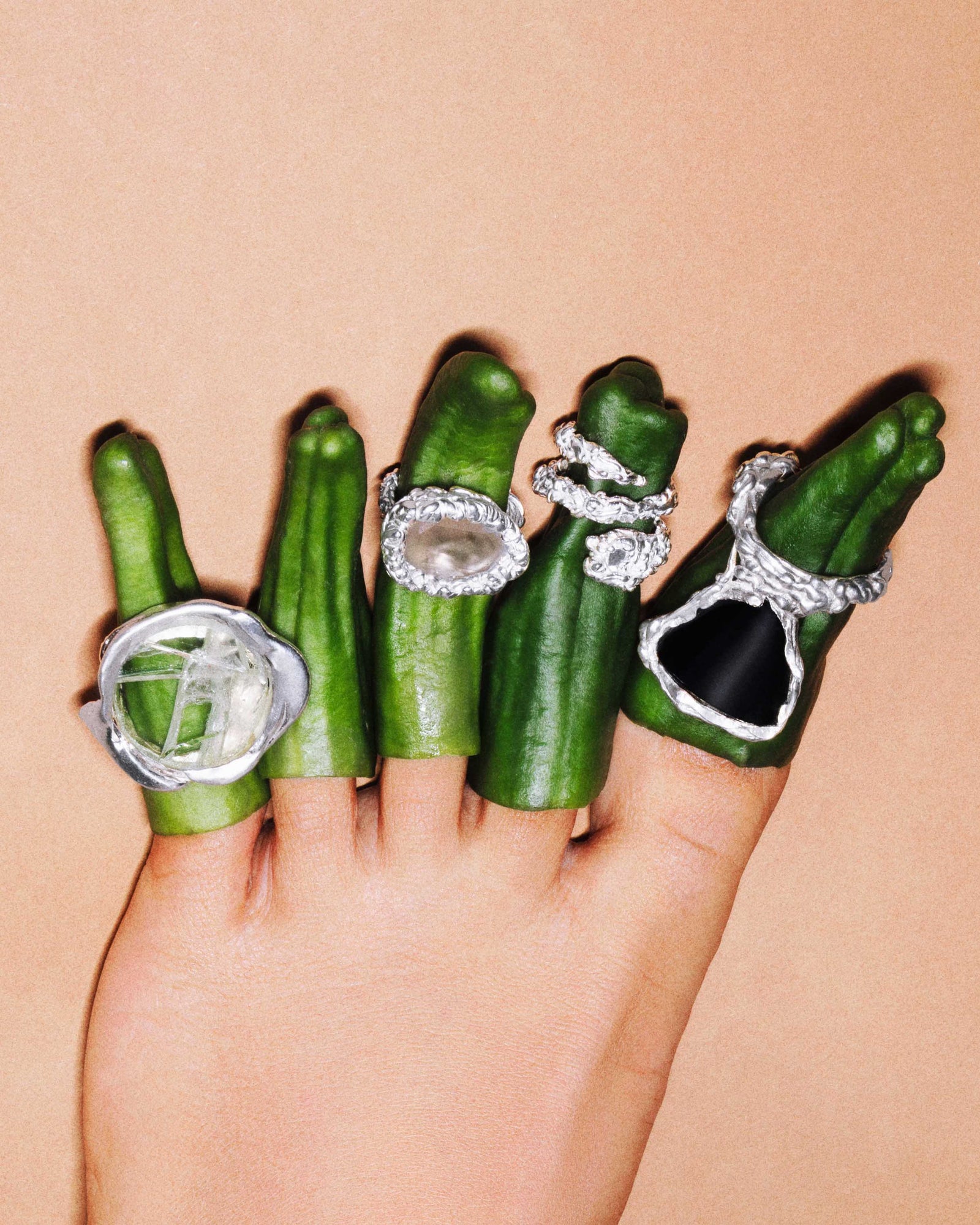 Silver YCCIJ rings on green peppers worn over the fingers of a hand