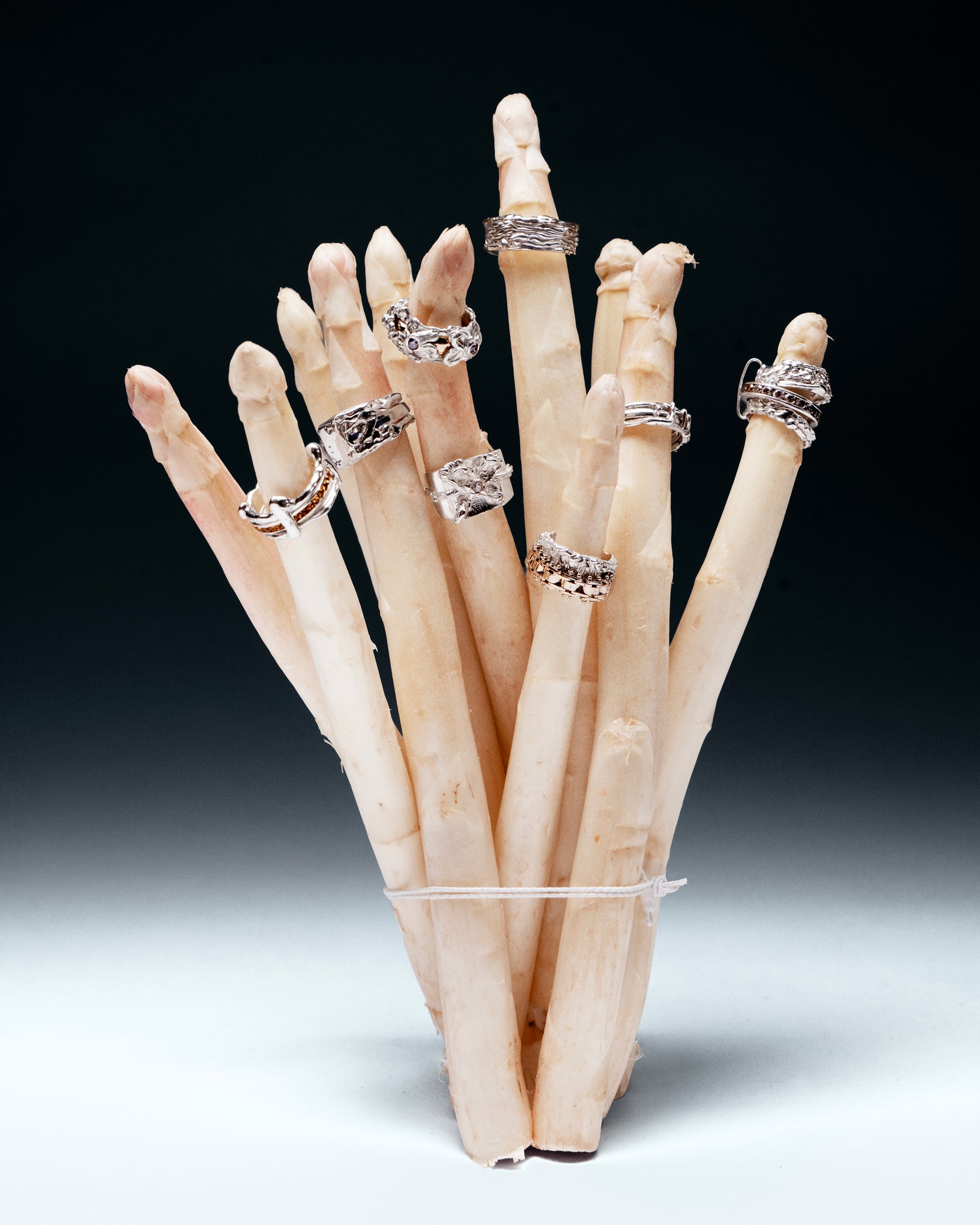 Silver YCCIJ rings arranged on a bundle of white asparagus